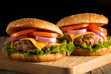Home made hamburger with beef, onion, tomato, lettuce and cheese. Fresh burger close up on wooden rustic table with potato fries, beer and chips. Cheeseburger.
