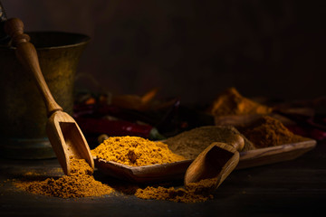 Various Indian spices with wooden spoons on a wooden table.