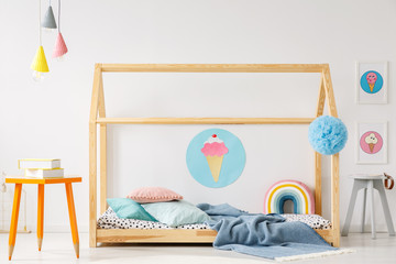 Orange table under colorful lamps next to wooden handmade bed in kid's bedroom interior