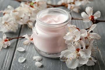 Fototapeta na wymiar Jar of cream and blooming flowers on wooden background