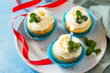 Colorful cupcake with whipped cream, poppy and orange peel on a blue a stone or slate background.