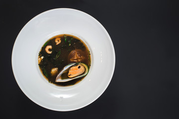 Tasty soup from seafood and mushrooms on black background
