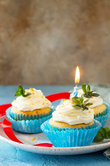Birthday cupcake with whipped cream, poppy and orange peel on a blue a stone or slate background. Copy space.