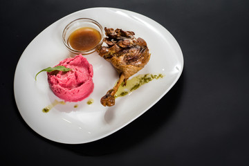 Fried chicken shin with sauce and pink potatoe puree on black background