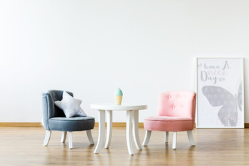 Pastel chairs at white table in girl's room interior with poster and copy space on the wall. Real...