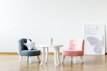 Pastel chairs at white table in girl's room interior with poster and copy space on the wall. Real photo