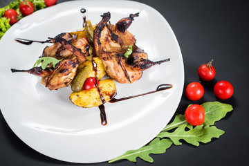 Grilled quail meat with vegetables on black background