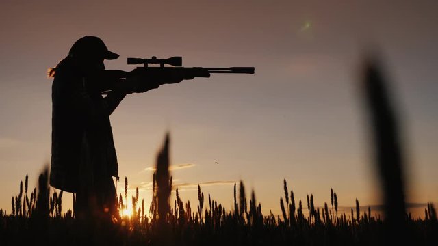 The hunter is aiming from a rifle with an optical sight. It stands in a picturesque place at sunset