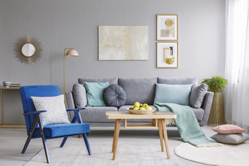 Blue armchair with pillows standing next to wooden table with fresh apples in grey living room...