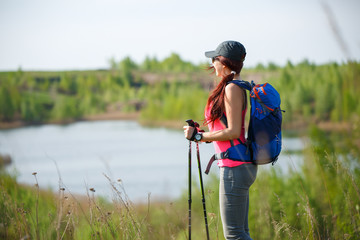 Photo of sporty woman with walking sticks on background of lake and green vegetation