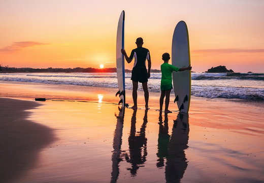 Father and son surfers stay on the sunset beach