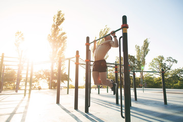  A young man pulls himself up in the park on a sports field.