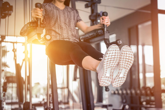 Woman performing hanging leg raises on gym fitness indoor with sunset. Showing strong abdominal