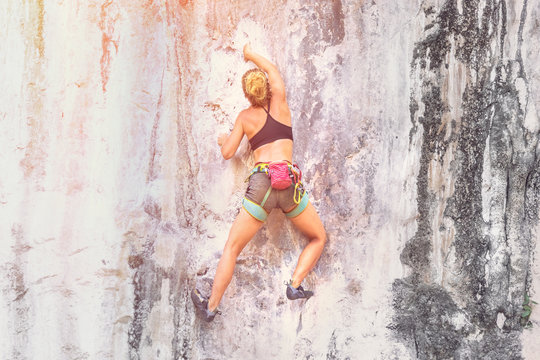 Young woman climbing a cliff without safety equipment on a summer day. Toned
