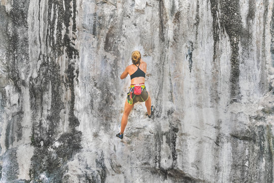 Young blond woman climber climbs on a rock without safety equipment