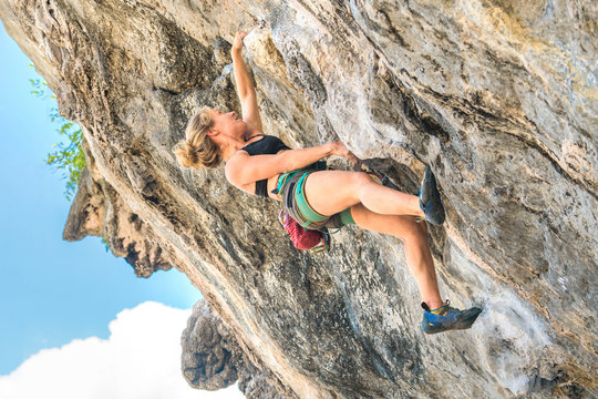 Young woman climbs on a overhanging cliff on a summer day