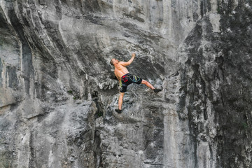 A young male athlete climbs up a cliff without a safety rope