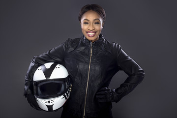 Motocycliste noire ou pilote de voiture de course ou cascadeuse portant une combinaison de course en cuir et tenant un casque de protection. Elle se tient en toute confiance dans un studio