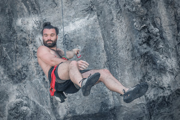 A bearded man climbers hanging on a safety rope in the mountains