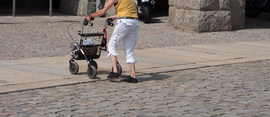 Alte Frau überquert eine Straße mit dem Rollator