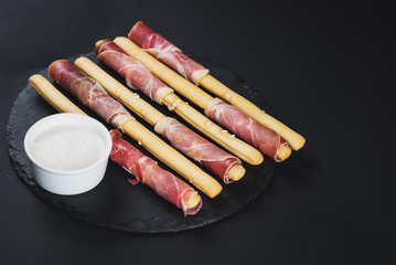 Bread sticks wrapped up by ham on black background