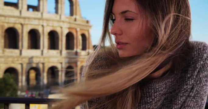 Beautiful woman with long brown hair blowing in the wind standing outside in Rome, Italy, Thoughtful and serious young lady looking to the side by Colosseum in Rome, 4k