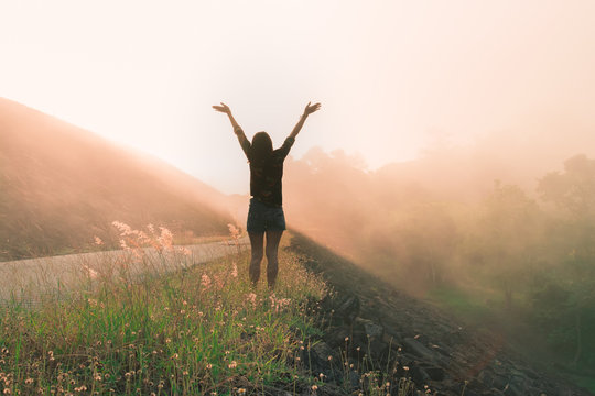 Back View Of Happy Young Woman Raise Arms With Beautiful Morning Sunrise Landscape, Travel Around The World Concept.