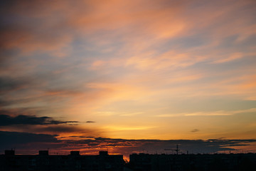 Beautiful cloudy dramatic morning sky above silhouette of city buildings. Picturesque dawn in city. Background of varicolored clouds. Unimaginable fantasy sunrise in heaven.