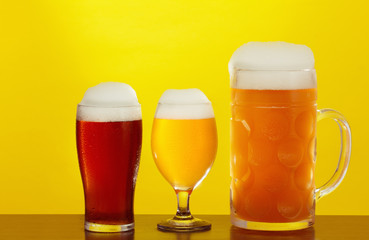 Mug and glass of beer close-up with froth over yellow background