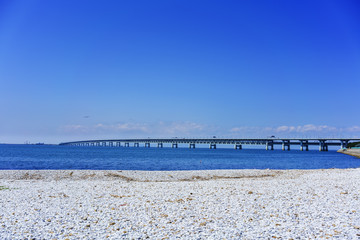 Beautiful artificial marble beach along the shoreline of Rinku Town , viewing Kansai kokusai kuko renraku-kyo ( toll road ) across blue sea of Osaka bay to Kansai International airport , Osaka , Japan