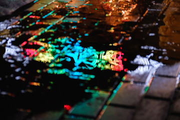 A puddle on a rainy night in the city with reflections of lanterns and advertising sign in blue tones