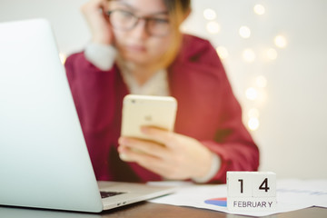 Business woman wearing red coat glasses still working in Valentine day.using notebook laptop ,smartphone on office desk and wooden calendar 14 February. Hard work, holiday festival.