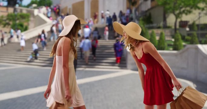 Pretty young blonde and brunette enjoying themselves while out exploring Rome, Italy, Two attractive white females in summer dresses and holding shopping bags spinning around near Spanish Steps, 4k