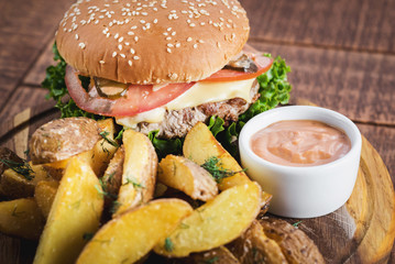 Tasty burger with fried potatoes on wooden board