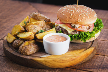 Tasty burger with fried potatoes on wooden board