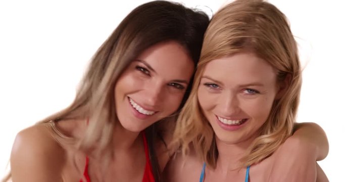 Portrait of two young white females posing happily together on white copy space, Attractive brunette with arm around blonde friend standing on white background, 4k
