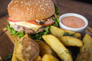 Tasty burger with fried potatoes on wooden board