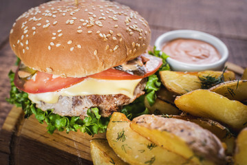 Tasty burger with fried potatoes on wooden board
