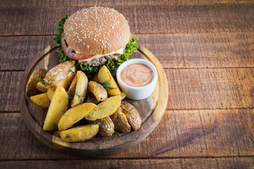 Tasty burger with fried potatoes on wooden board