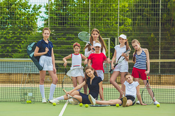 Portrait of group of girls as tennis players holding tennis racket against green grass of outdoor court