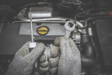 Car mechanic hands in protective gloves holding a wrench and screwdriver in the garage. Ready to repair engine. Car motor repair. Problems and solutions concept.