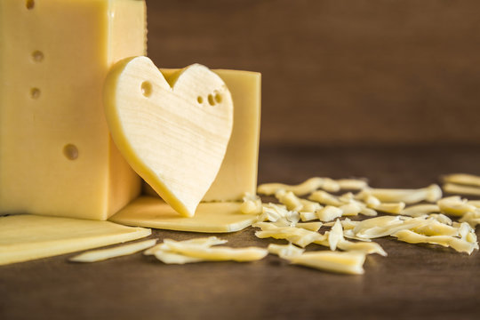 Fresh, yellow cheese with heart shape and grated slices on the rustic brown wooden table in the kitchen. Farm's natural dairy product. Healthy food. Empty place for text or a logo.