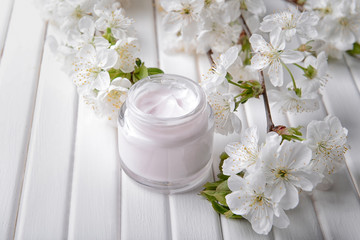 Jar with cream and blooming flowers on table