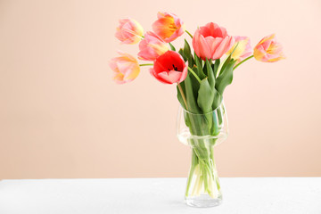 Vase with beautiful tulips on table against color background