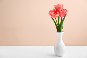 Vase with beautiful tulips on table against color background