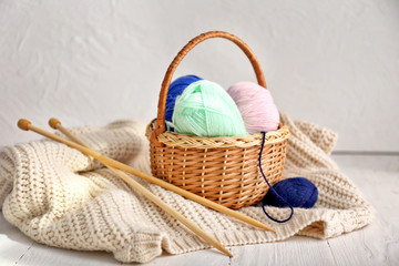 Wicker basket with knitting yarn, clothes and needles on table