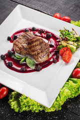 Grilled meat steak with raspberrie sauce on wooden background