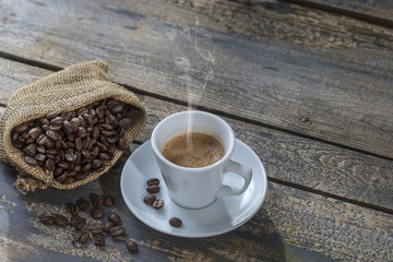 white cup of steamingcoffee and sackwith beans on table, top view