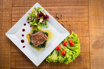 Fried piece of meat with herbs and spices on wooden background