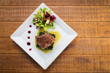Fried piece of meat with herbs and spices on wooden background